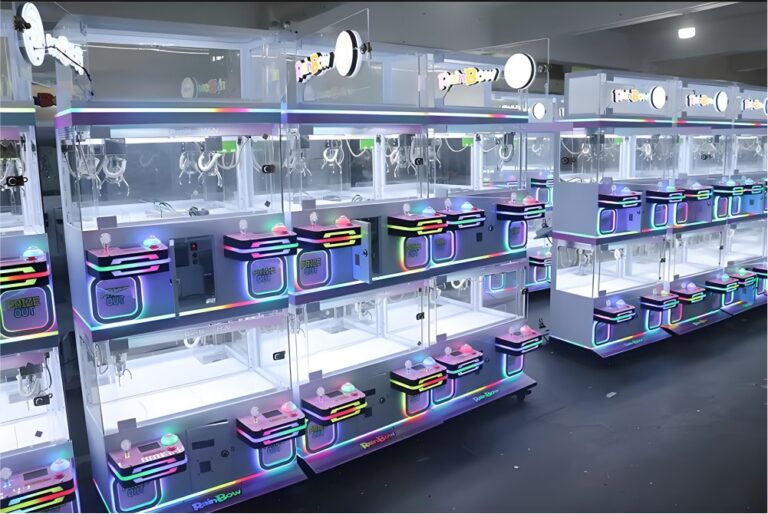 Plusieurs machines à pinces blanches LeYou " Rainbow " avec lumières circulaires au plafond, panneaux LED colorés (rose/bleu/violet) et affichages " PRIZE OUT " sous un éclairage d'arcade lumineux.